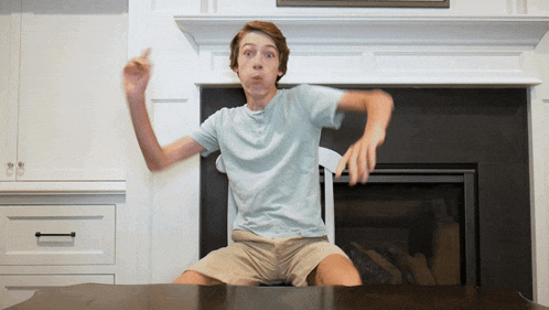 a young boy is sitting on a table in front of a fireplace and making a funny face