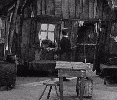 a black and white photo of a man standing in front of a window in a wooden house .