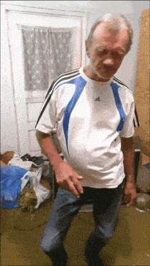 a man in a blue and white adidas shirt stands in a room