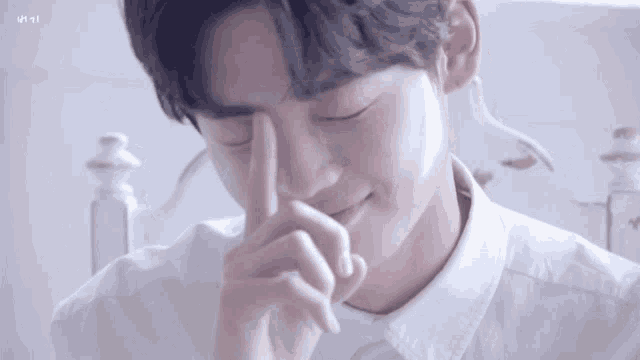 a young man in a white shirt covering his face with his hand