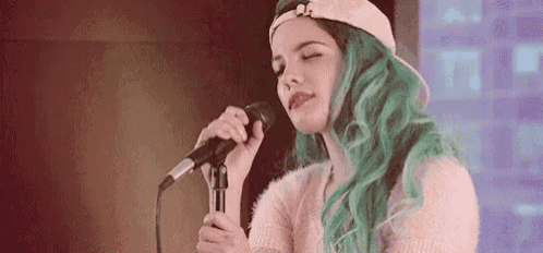 a woman with green hair is singing into a microphone while wearing a baseball cap .