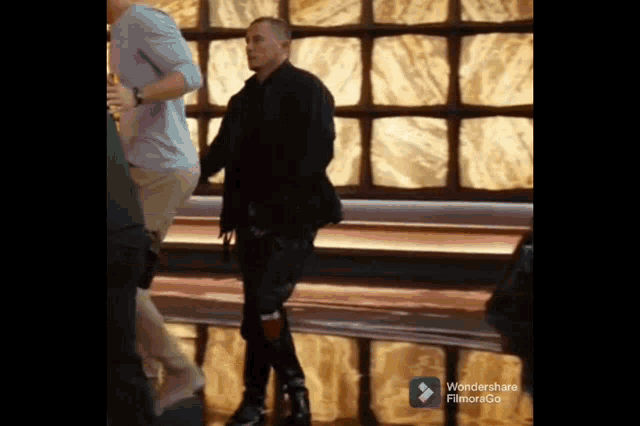 a man in a black jacket is walking in a room with a wondershare filmora go watermark