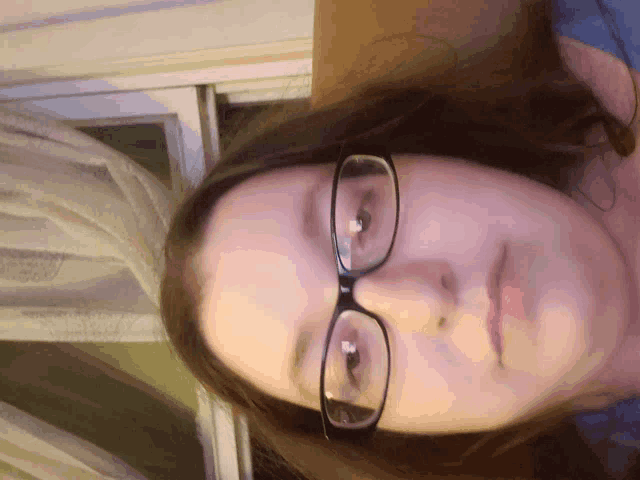 a woman wearing glasses and a blue shirt looks down at the camera