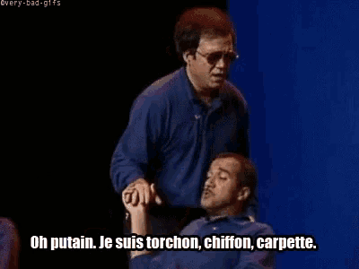 a man in a blue shirt is talking to another man in a blue shirt who is sitting in front of him .