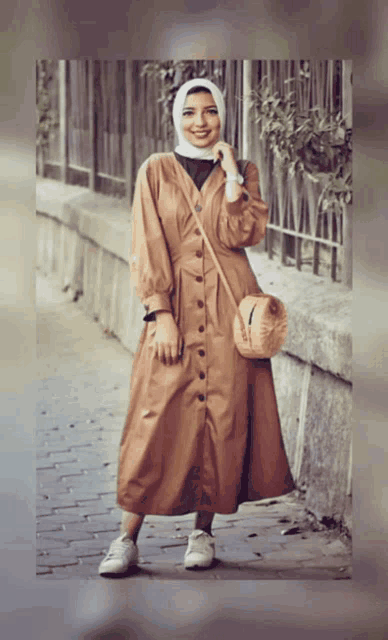 a woman wearing a hijab and a brown dress holds a purse