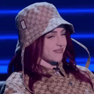 a woman wearing a hat and a gucci shirt is sitting on a stage .