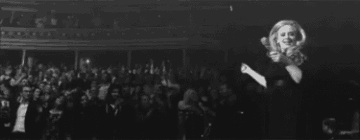 a black and white photo of a woman holding a microphone in front of a crowd in a theater .