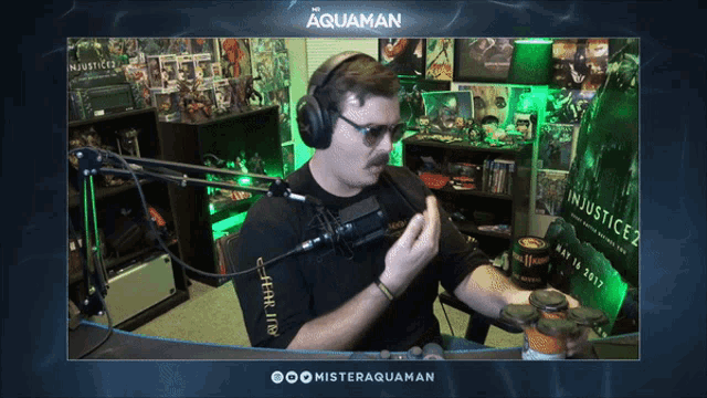 a man wearing headphones talks into a microphone in front of a screen that says aquaman