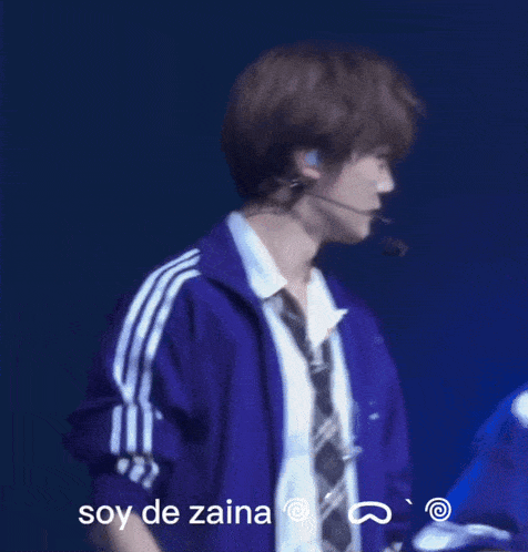 a man in a purple jacket and tie is standing in front of a sign that says soy de zaina