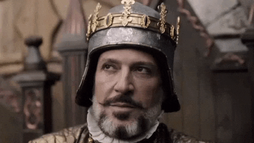 a man with a beard and a crown on his head is wearing a helmet .