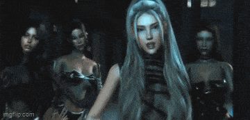 a woman with long hair is dancing in front of a group of women in a dark room .
