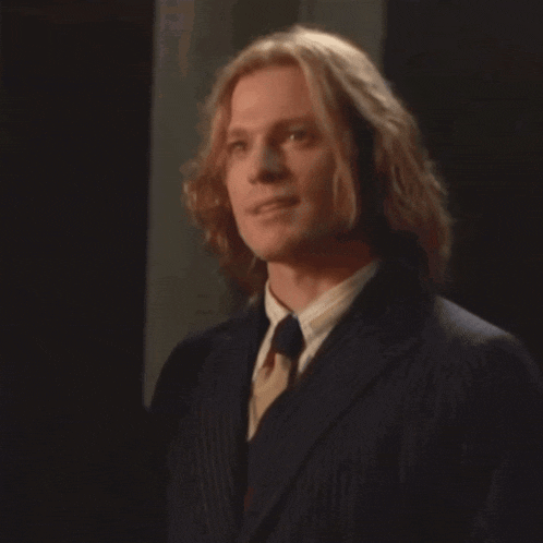 a man with long blonde hair is wearing a black suit and tie