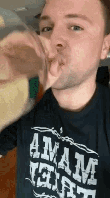 a man wearing a black shirt with the word anam on it is drinking from a glass
