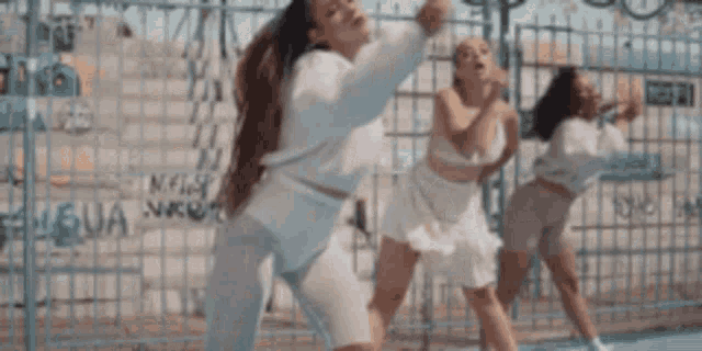a group of women are dancing together in front of a fence .