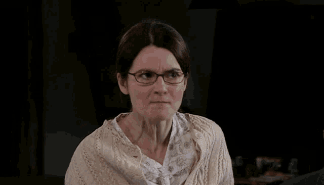 a woman wearing glasses and a sweater looks angry