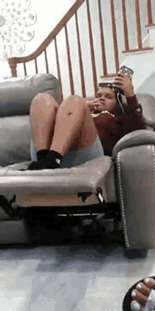 a woman is sitting on a couch with her legs crossed while holding a cell phone .