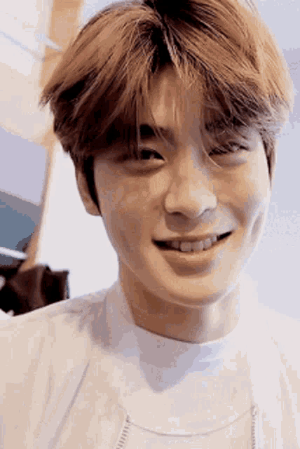 a close up of a young man 's face with a white shirt on smiling .