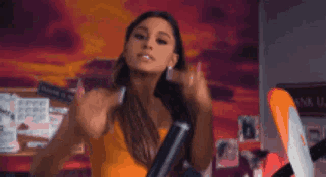 ariana grande is wearing a yellow tank top and holding a microphone in a room .