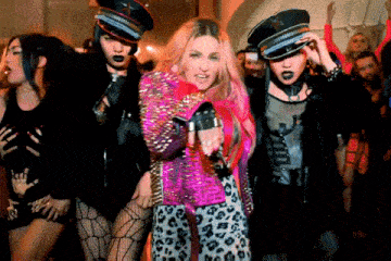 a woman in a pink jacket and leopard print pants is singing into a microphone in front of a crowd