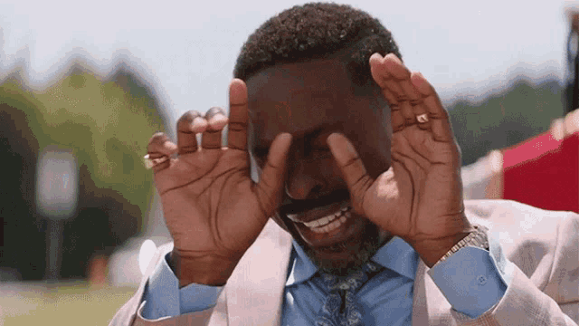a man in a suit and tie is covering his eyes with his hands while smiling .