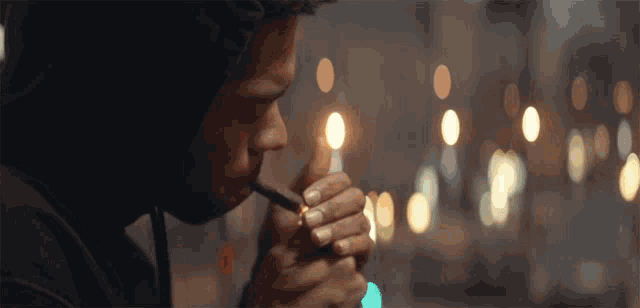 a man in a black hoodie is lighting a cigarette