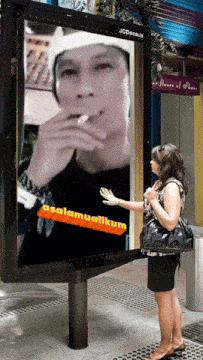 a woman stands in front of a large billboard that says assalamualikum