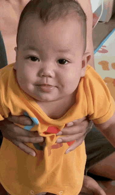 a baby in a yellow shirt is being held by a woman