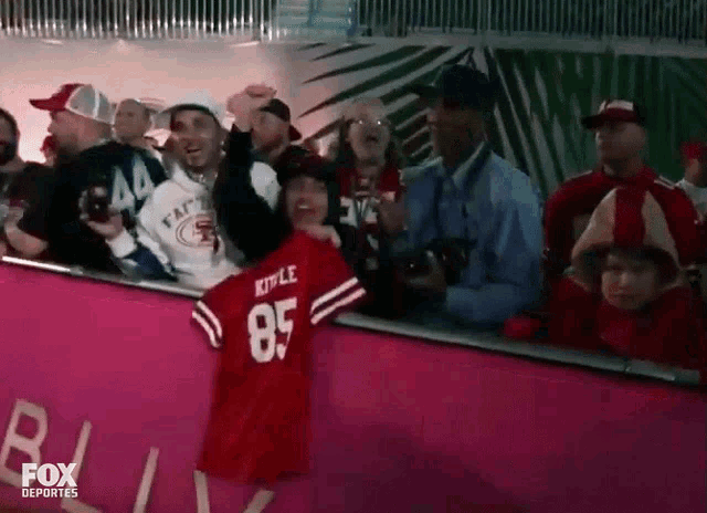 a kid wearing a kyle 85 jersey stands in a crowd of people