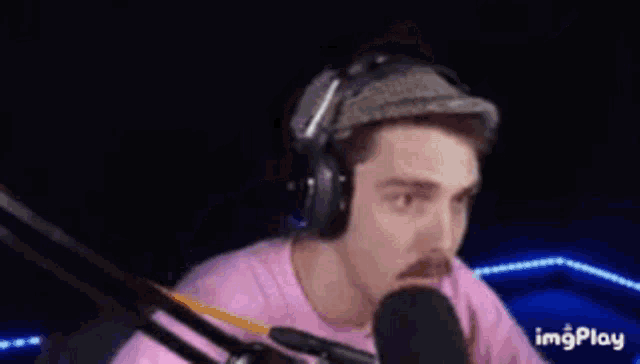 a man wearing headphones and a pink shirt is sitting in front of a microphone and saying impostor time .