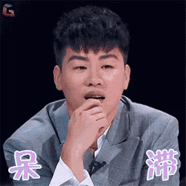 a young man in a suit is making a funny face with his hand on his chin .