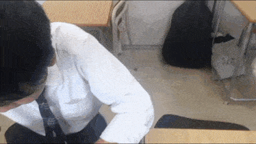 a man in a white shirt and tie sits at a desk in a classroom with a bag that says wrap on it