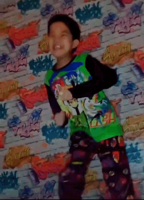 a boy wearing a green ben 10 shirt is dancing in front of a wall with graffiti on it