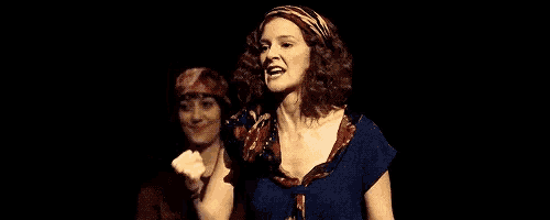a woman is flexing her muscles in a dark room while another woman looks on .