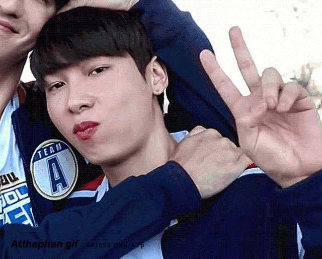 a man wearing a blue jacket with the letter a on it giving a peace sign