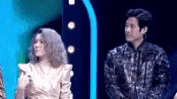 a man and a woman are standing next to each other on a stage . the woman is wearing a gold dress .