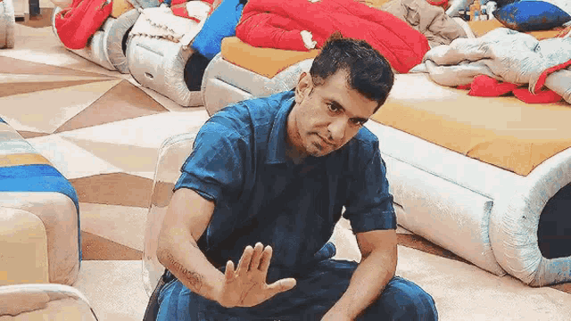 a man in a blue shirt is sitting in front of a row of beds making a stop sign