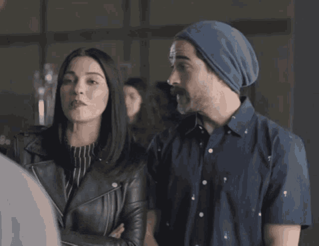 a man wearing a blue hat and a woman wearing a leather jacket are standing next to each other