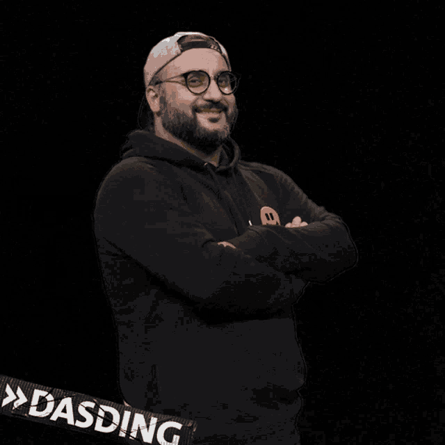 a man with a beard and glasses is giving a thumbs up and has a dasding sticker on his sleeve