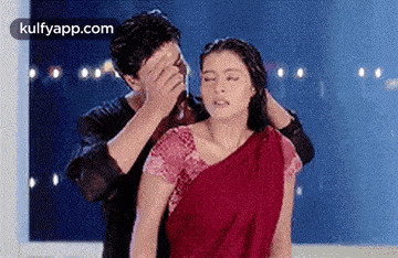 a man is covering his face while a woman in a red saree is standing next to him .