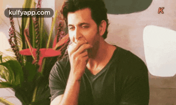 a man is covering his mouth with his hand while sitting in front of a flower arrangement .