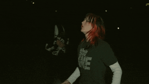 a woman with red hair and black bangs is wearing a black shirt that says the time .