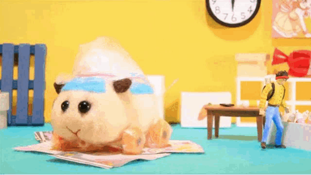 a stuffed animal is sitting on top of a magazine next to a table and a clock .