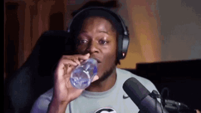 a man wearing headphones is drinking water from a plastic bottle .