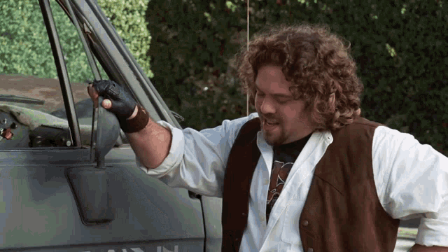 a man with curly hair stands in front of a van that says ' ain ' on it
