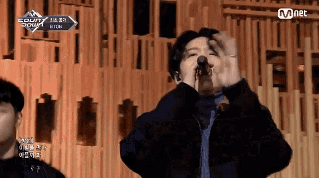 a man singing into a microphone in front of a wooden wall that says mnet