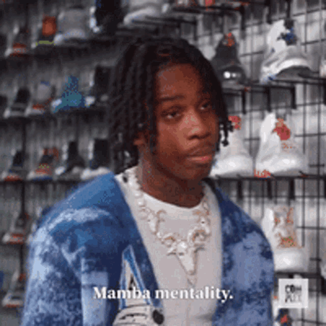 a young man wearing a blue sweater and a necklace stands in front of a wall of shoes .