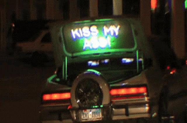 a car with the trunk open has a neon sign that says " kiss my ass "