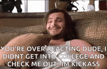 a man is sitting on a couch with a pillow and a caption that says you 're over reacting