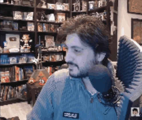 a man with a beard is sitting in front of a microphone in a room with shelves full of books .