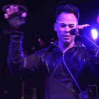 a man singing into a microphone in a dark room with purple lights